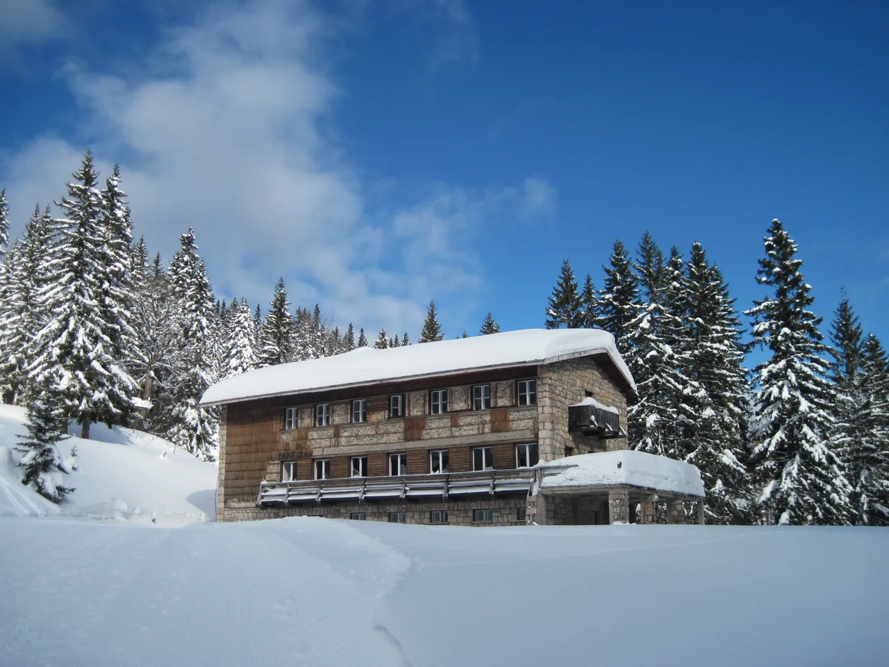 A stone and timber mountain hotel on Jahorina buried in deep snow under a blue sky