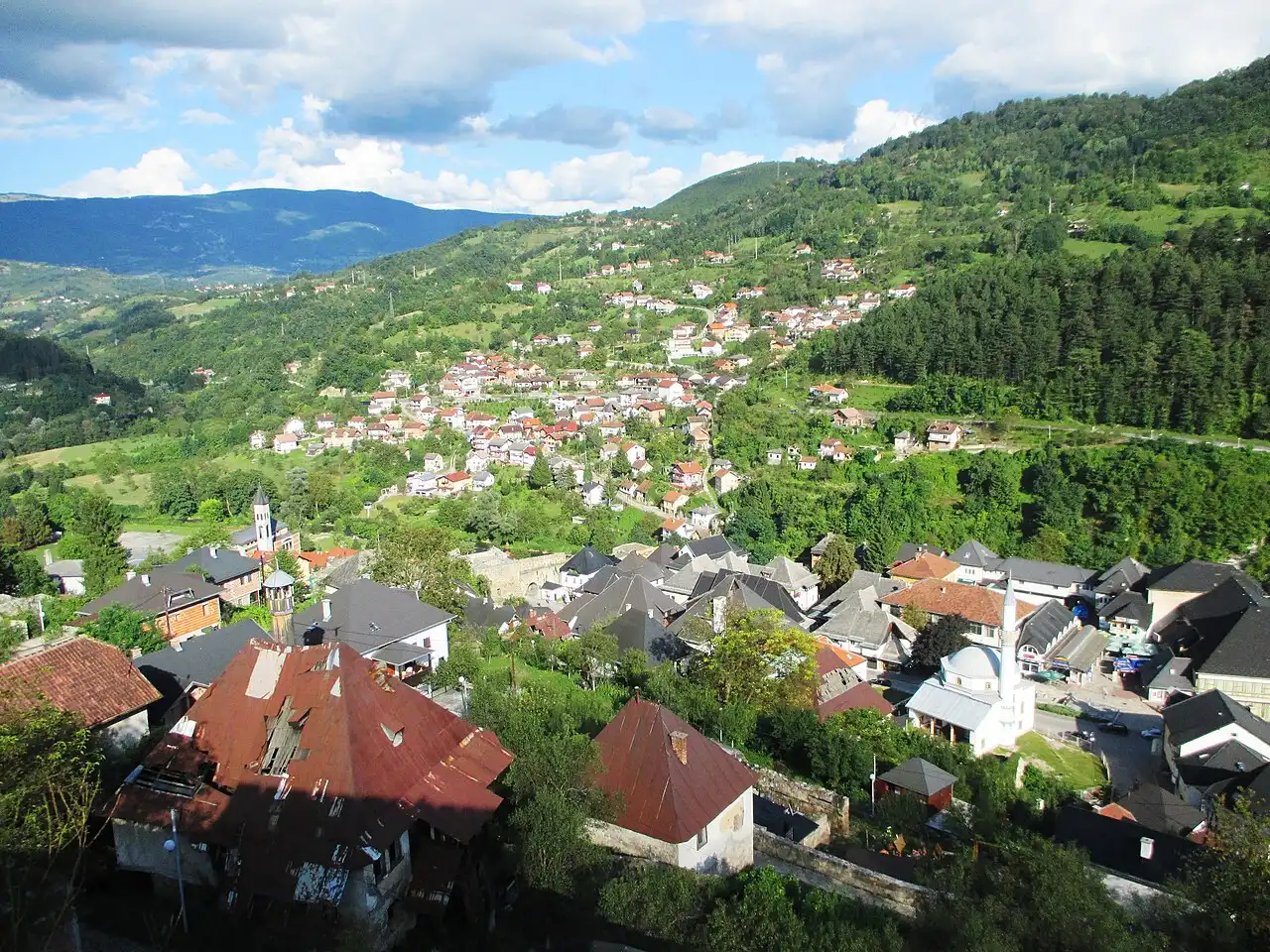 A wide view over Jajce and the green Pliva valley with hills in the distance