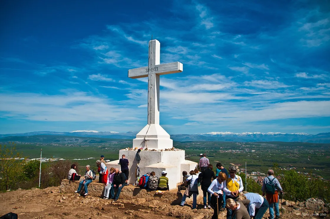 A white cross on a rocky hillside above Medjugorje with the village and vineyards below
