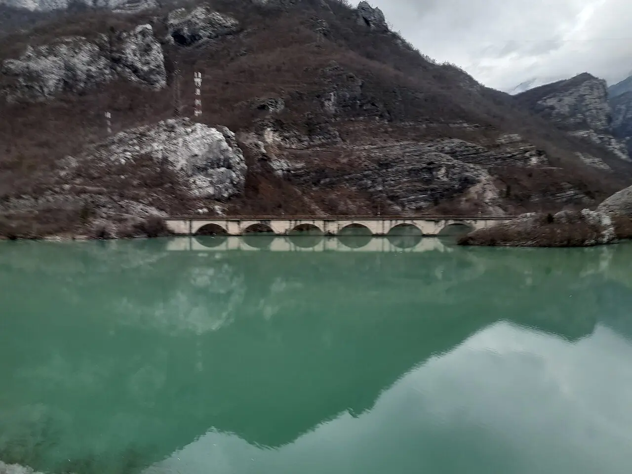 The green Neretva at the mouth of Diva Grabovica, a stone railway viaduct crossing the water below steep grey limestone walls of Cvrsnica