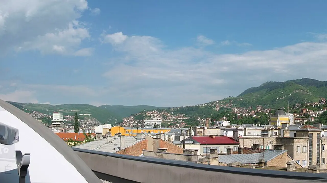 Sarajevo spread across its valley below Mount Trebević, red roofs and minarets under green hills, the destination of the route from Zagreb